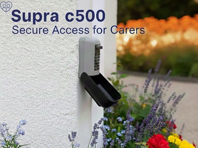Supra C500 Police Preferred keysafe fitted to an exterior wall by Pentland Locksmiths, surrounded by blooming flowers for discreet access by carers.